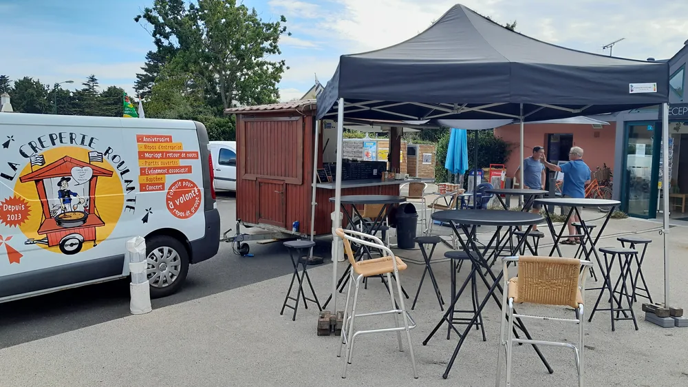 Mange-debout et tabourets installés sous et autour du barnum, devant la roulotte en bois