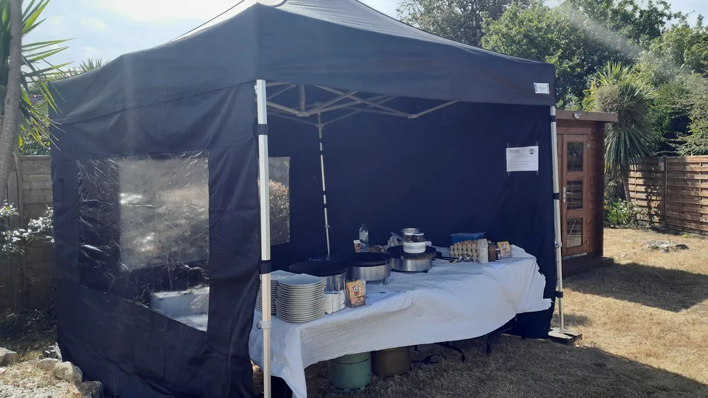 Stand de crêpes de La Crêperie Roulante sous un barnum noir, dans un jardin : billigs et assiettes sur une table nappée de blanc
