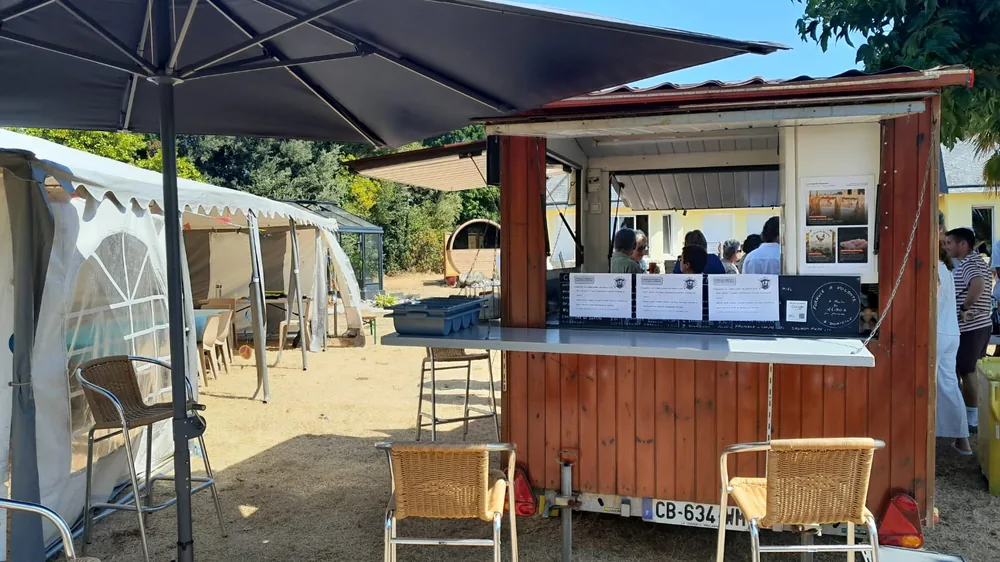 Roulotte à crêpes sous un grand parasol, à côté d'une tente de réception, des invités au comptoir