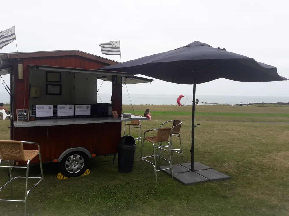Roulotte à crêpes sur une pelouse en bord de mer, drapeaux bretons au vent